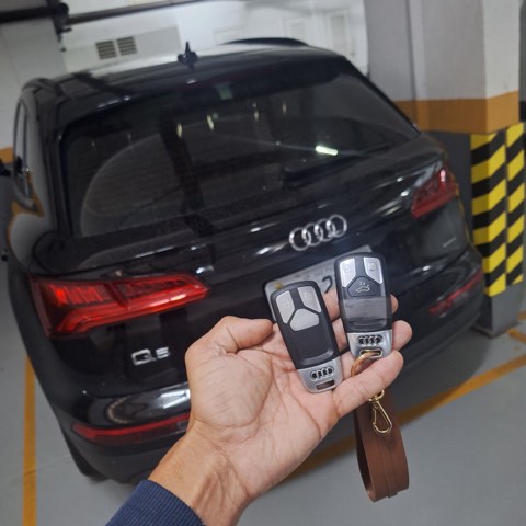 Chaveiro segurando duas chaves presenciais de Audi Q5 em frente ao veículo, após atendimento no local.