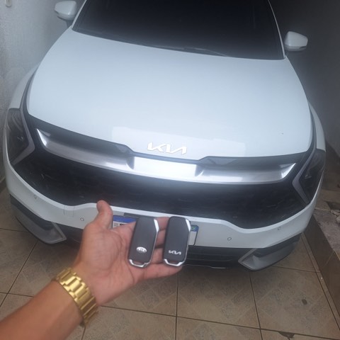 Duas chaves de Kia Sportage prontas, seguradas em frente à frente do veículo branco.
